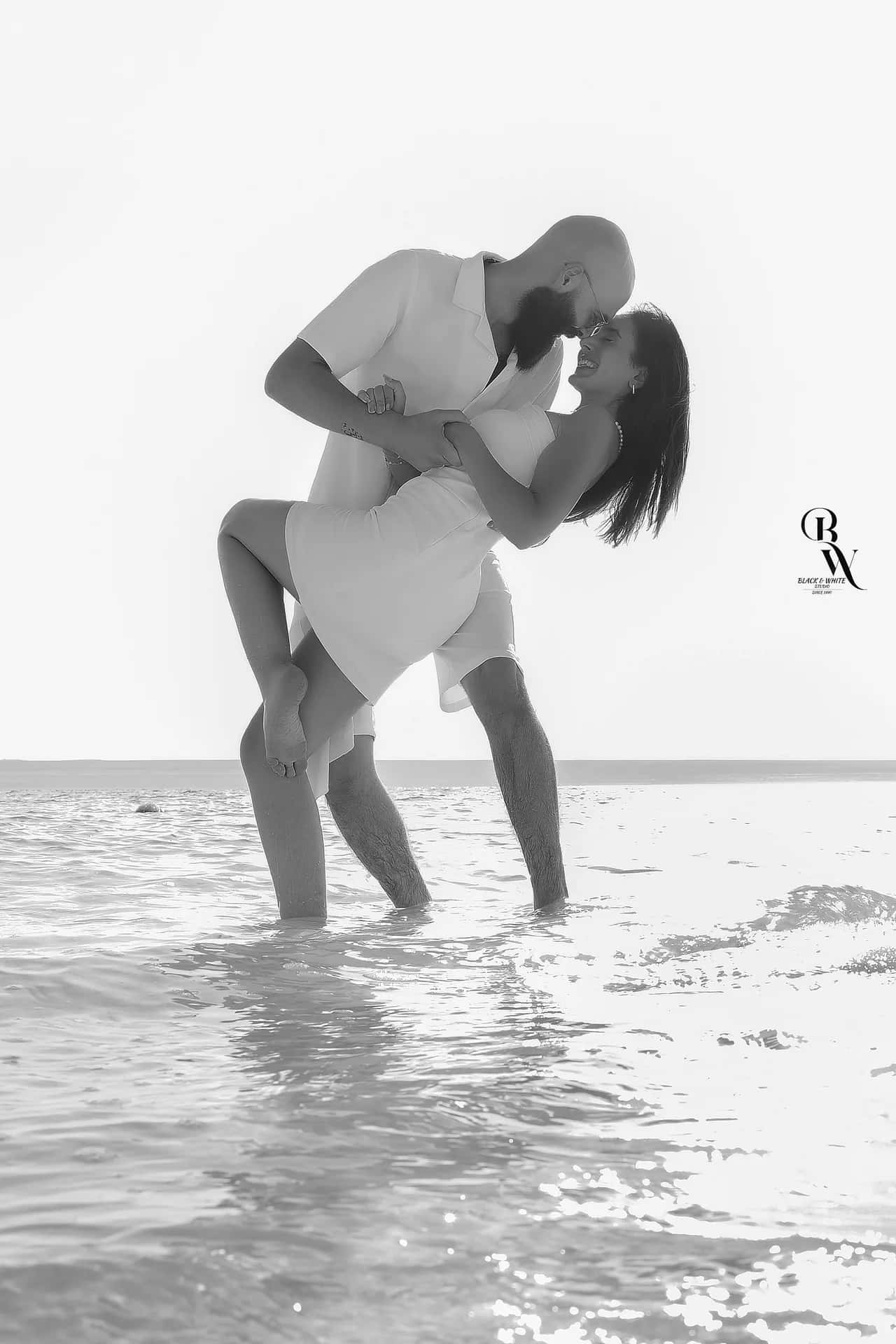 A man dipping his partner in the shallow water, in black and white