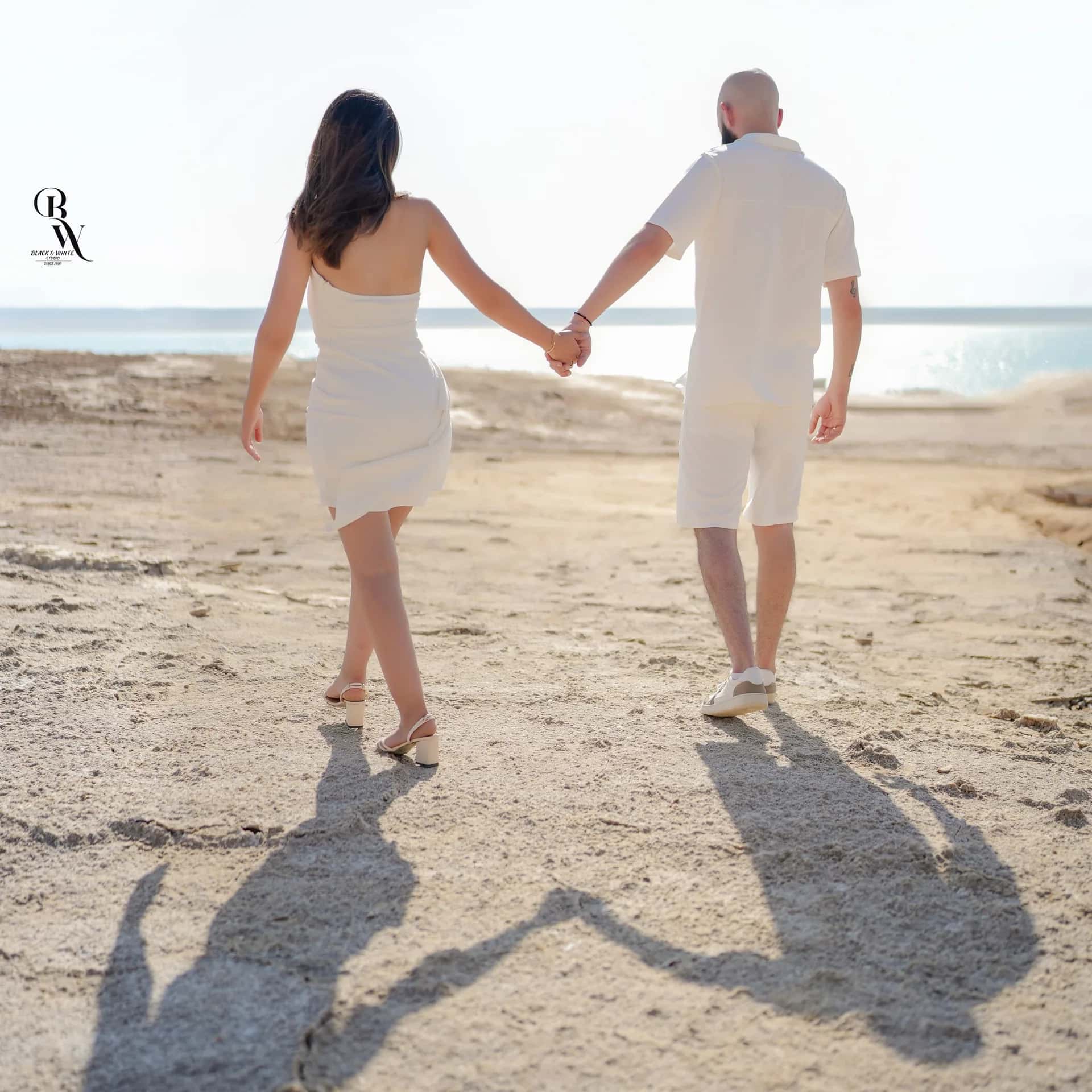 A couple walking along the bright shore, their shadows long