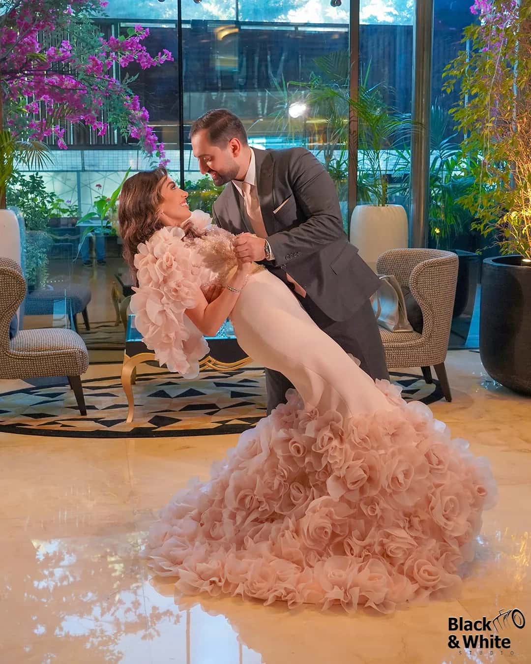 A groom dipping his bride in a pink gown on a terrace
