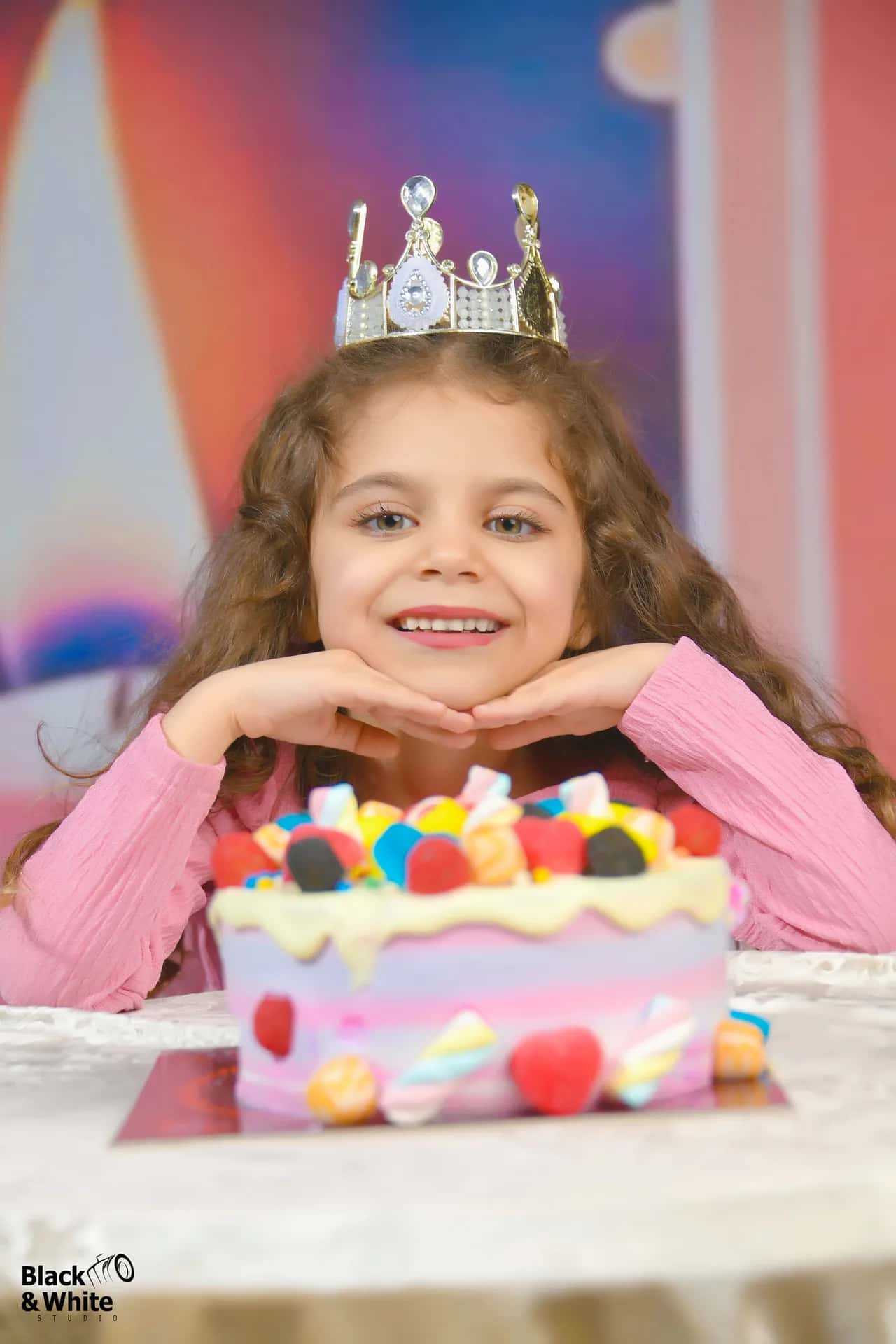 A little girl in a crown behind her birthday cake