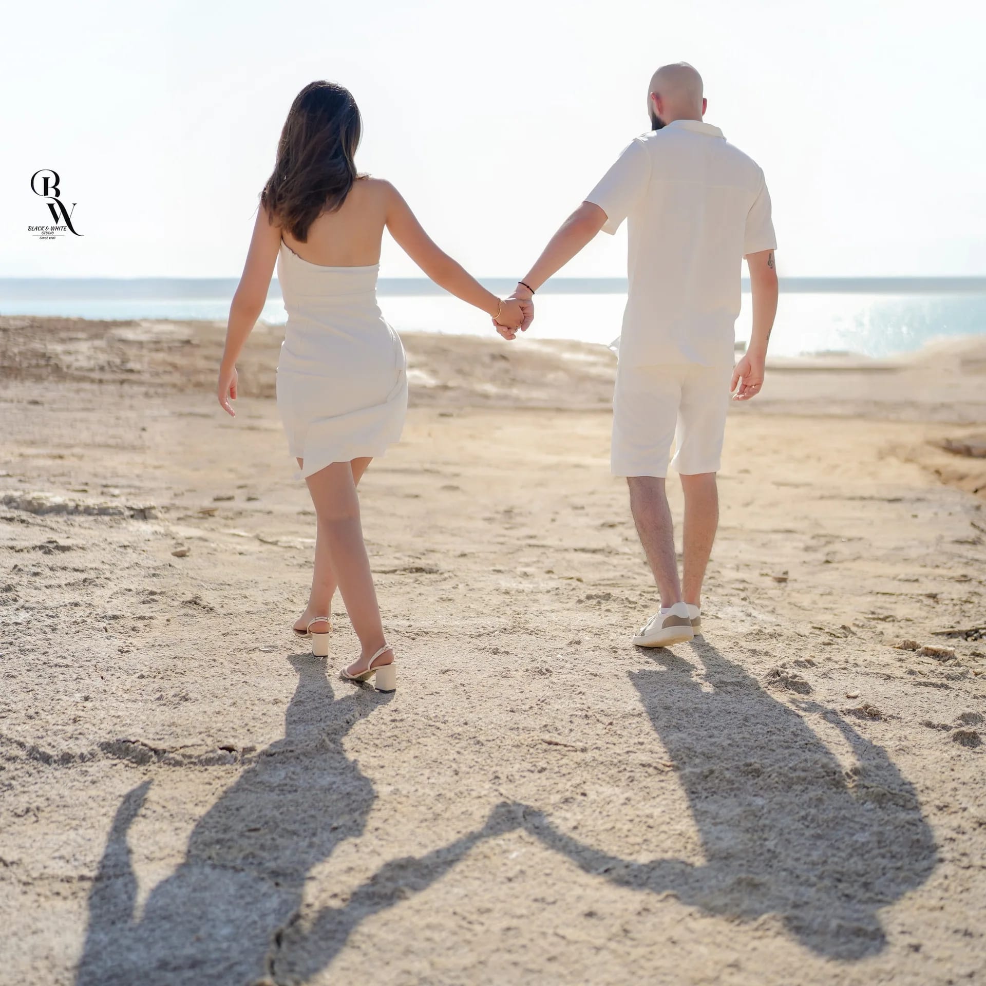 A couple walking along the bright shore, their shadows long