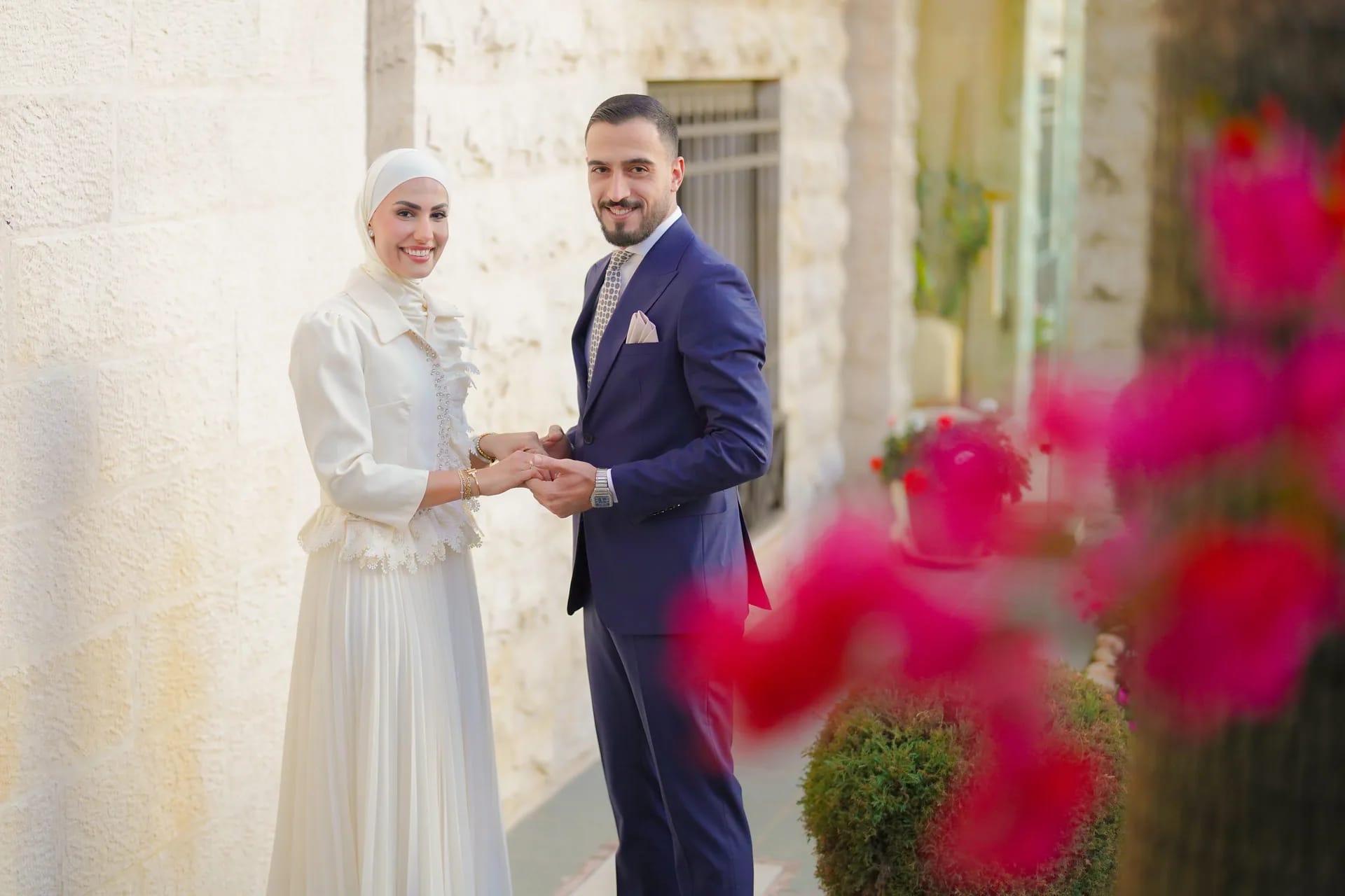 A couple holding hands behind a spray of pink flowers