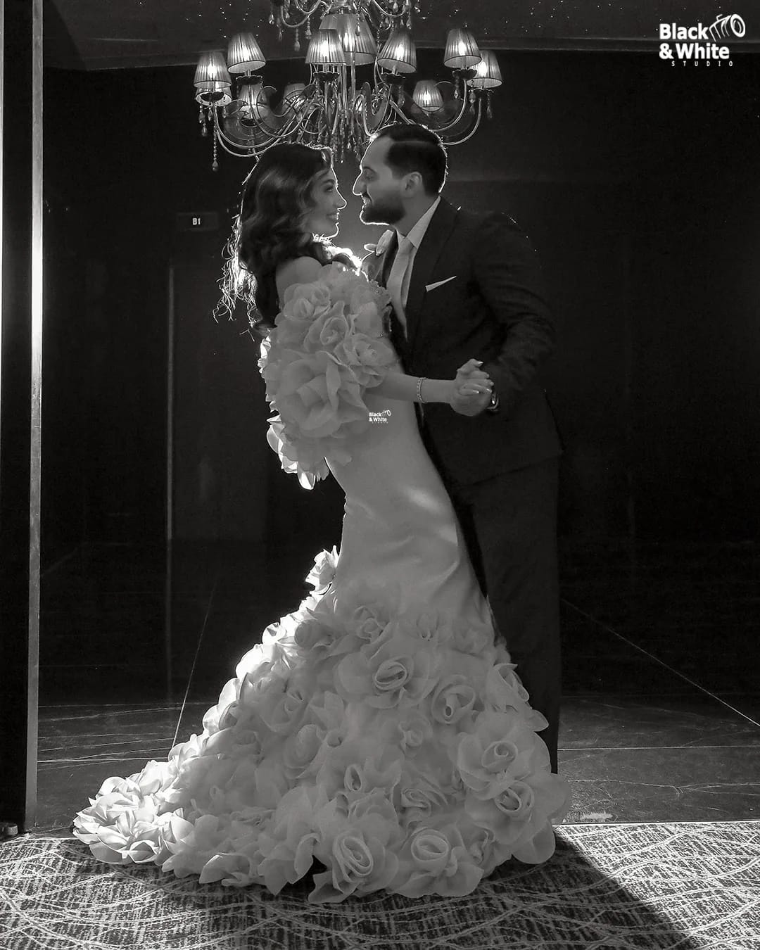 A couple dancing under a chandelier, in black and white