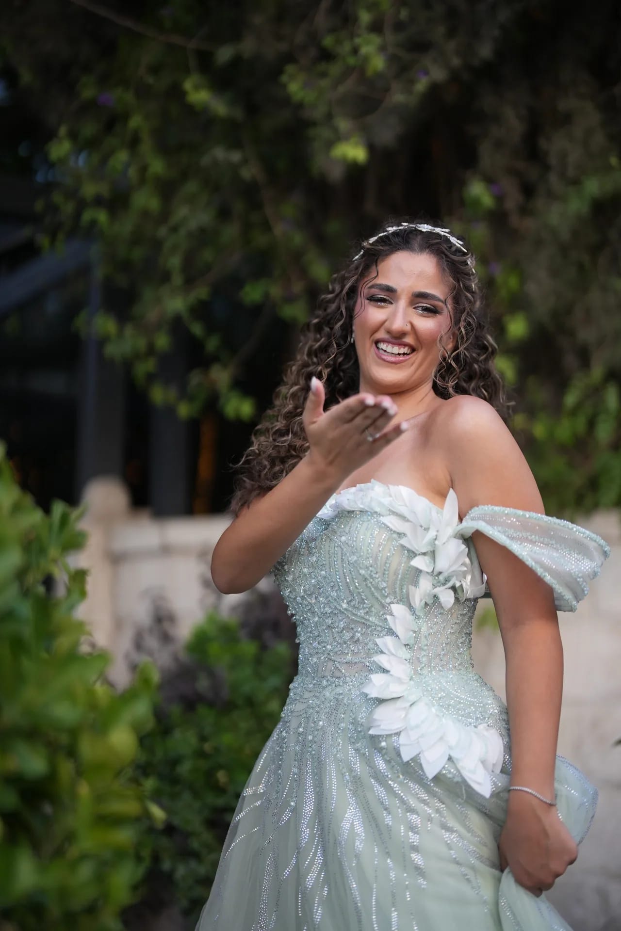 A bride in a mint gown blowing a kiss, laughing, among garden greenery