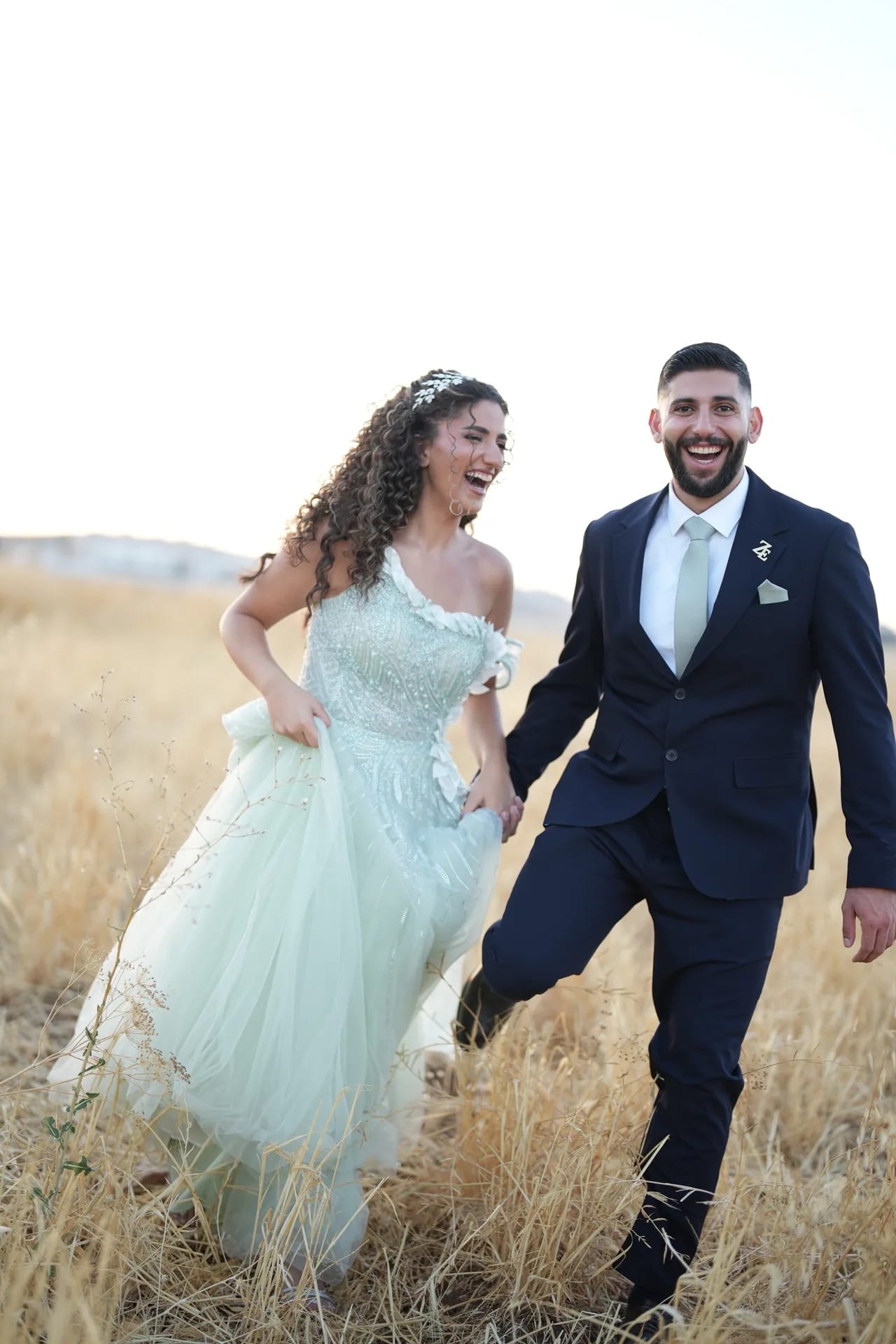 A couple laughing as they run hand in hand through a wheat field at golden hour