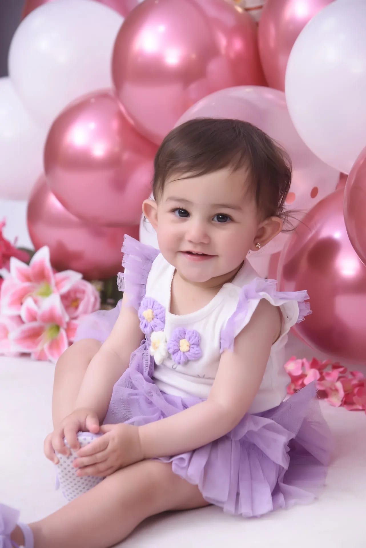 A baby sitting among pink and white balloons