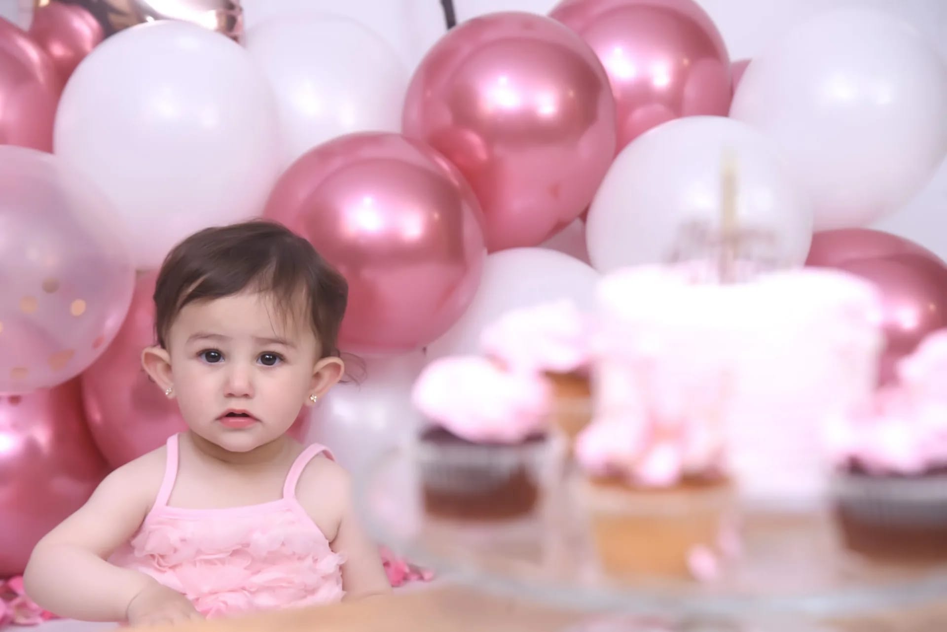 A baby beside cupcakes at a first-birthday shoot