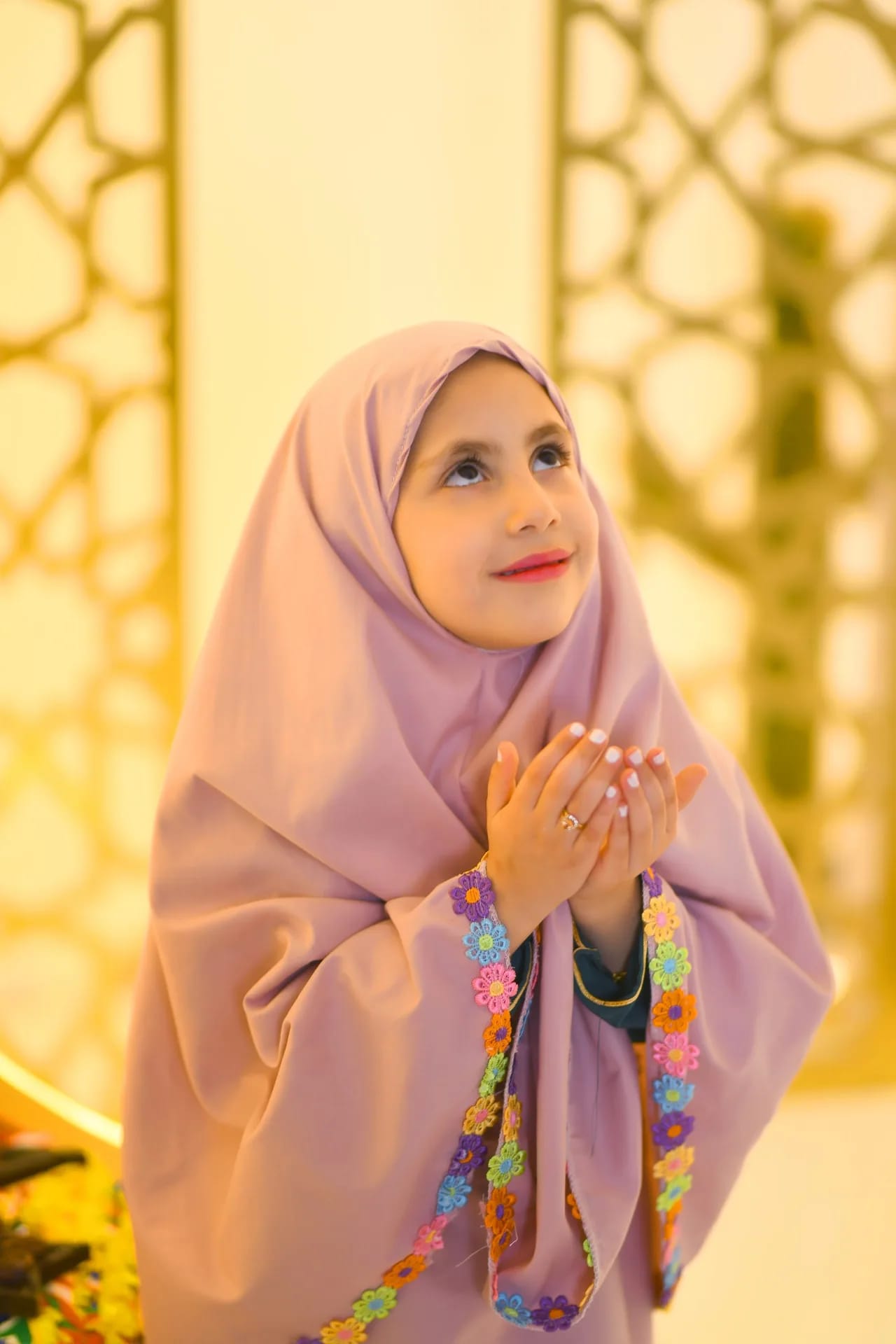 A girl in a pink hijab with her hands raised in prayer