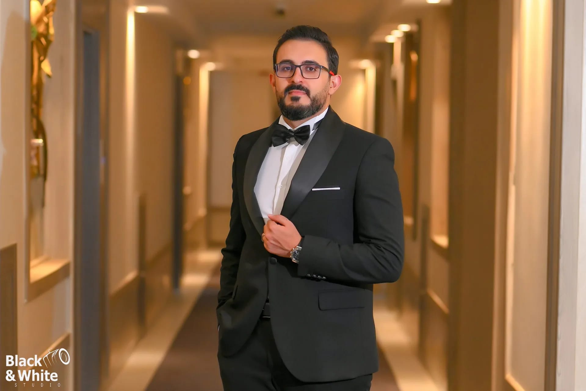 A groom in a tuxedo in a warmly lit hotel corridor