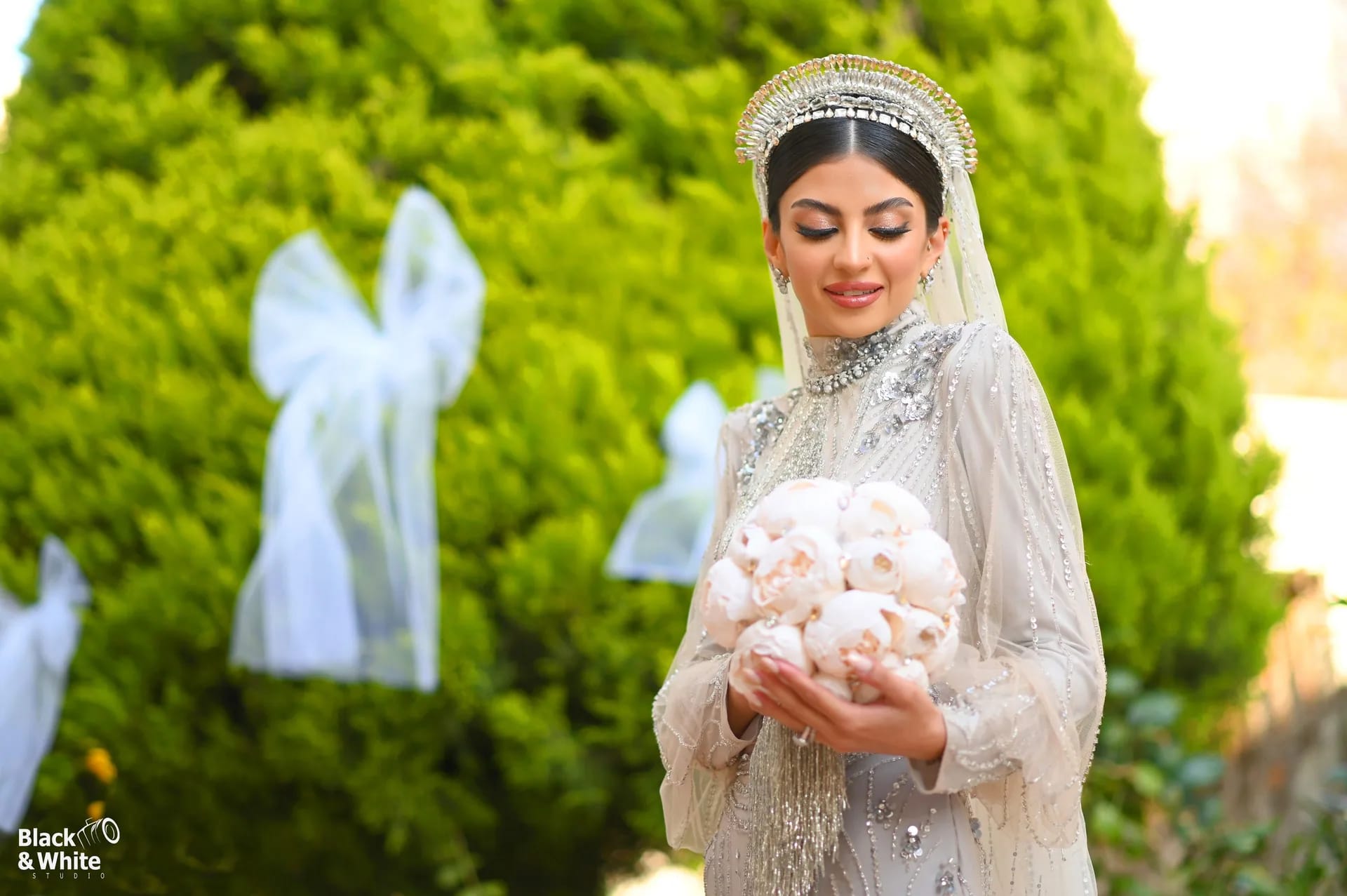 A bride in a crown holding a bouquet in a green garden