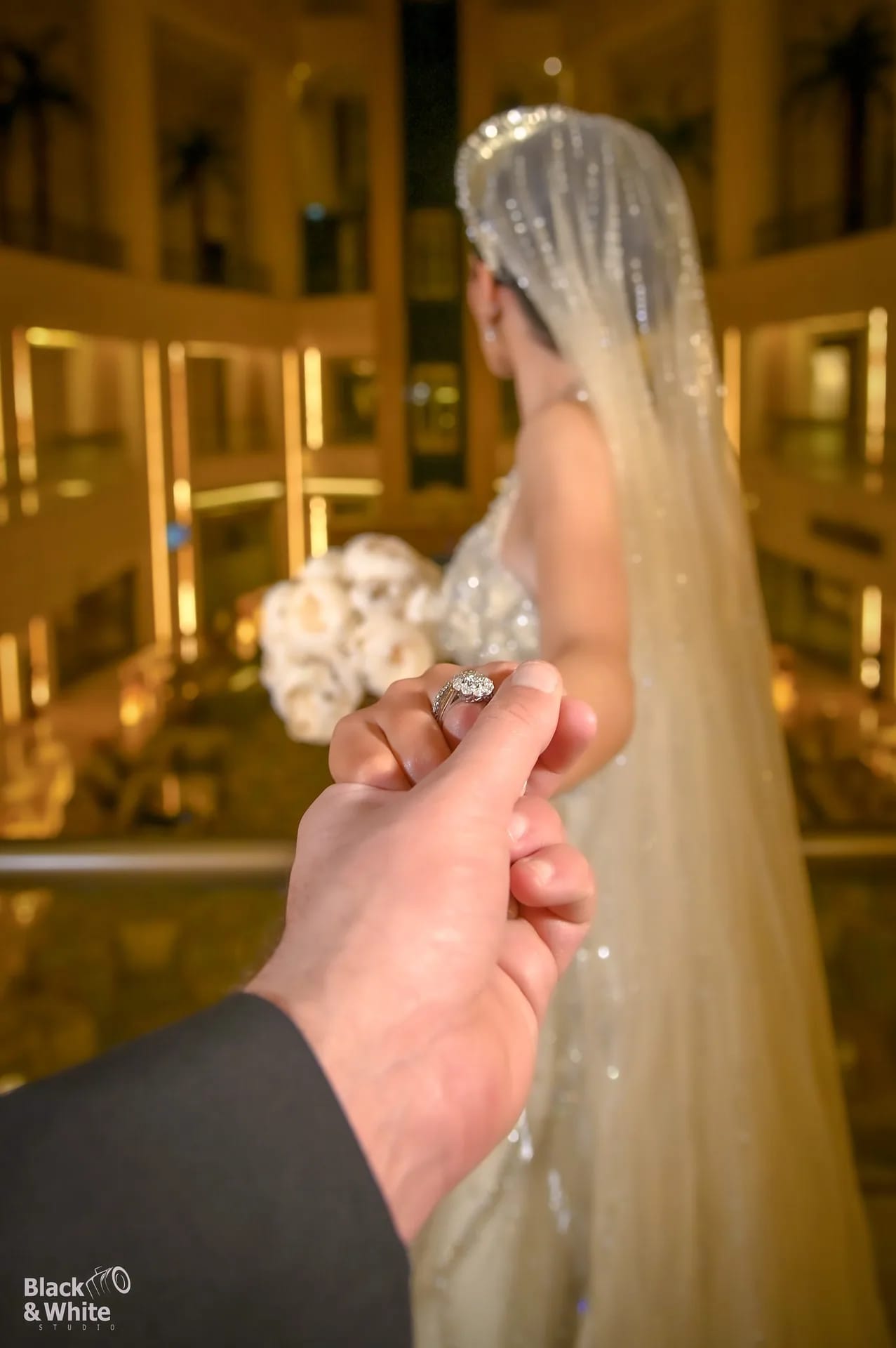 A groom holding his bride's hand under warm hotel lights