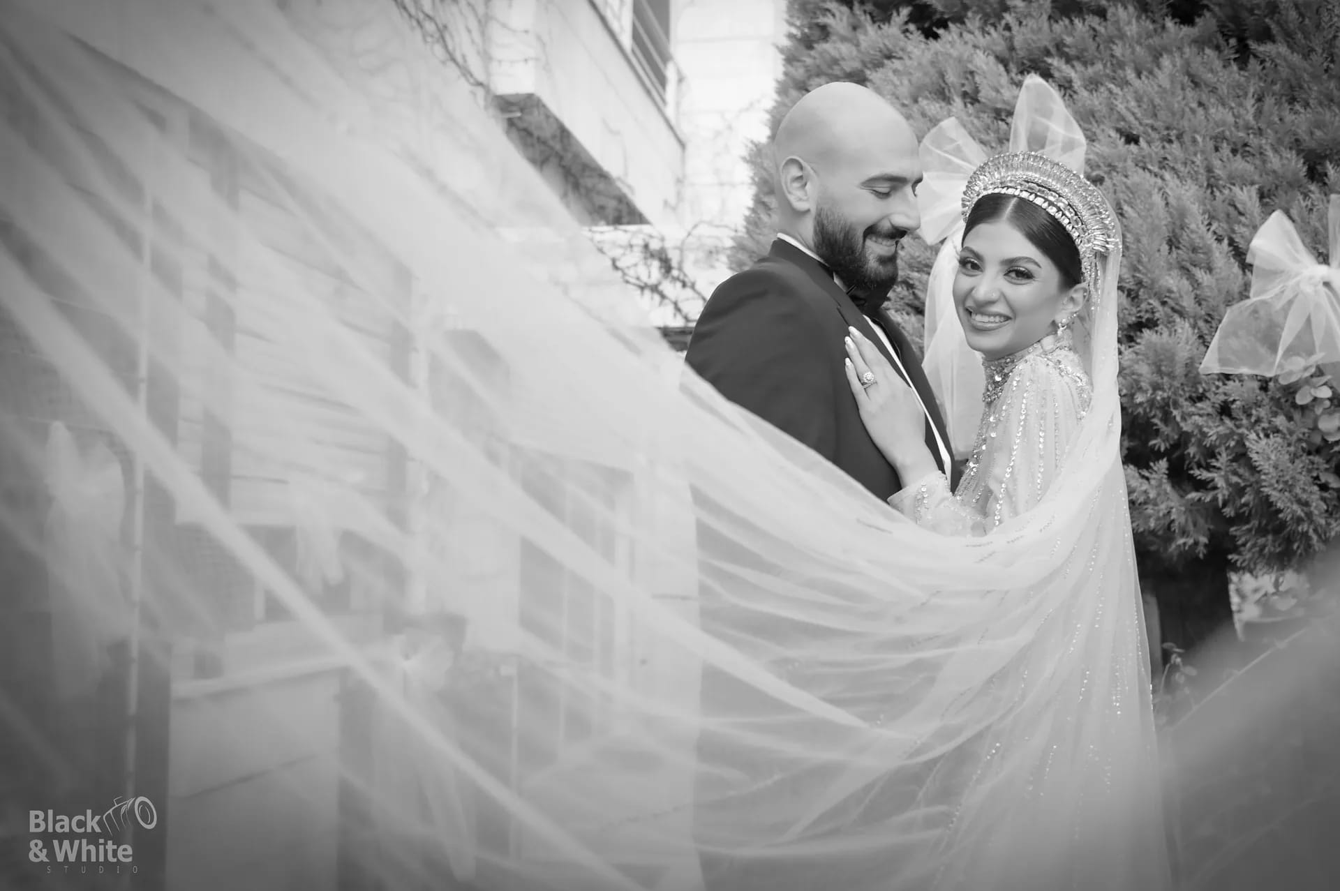 A couple inside a sweep of veil, in black and white