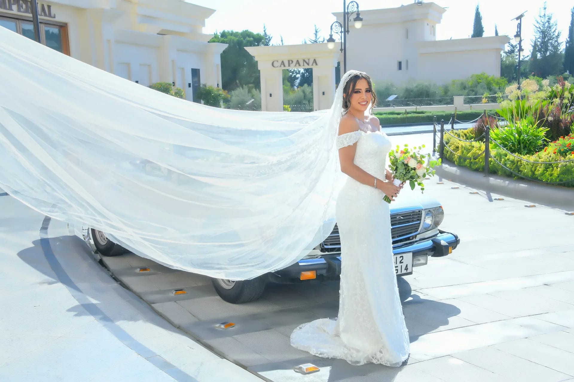 A veil streaming across the street beside a vintage car