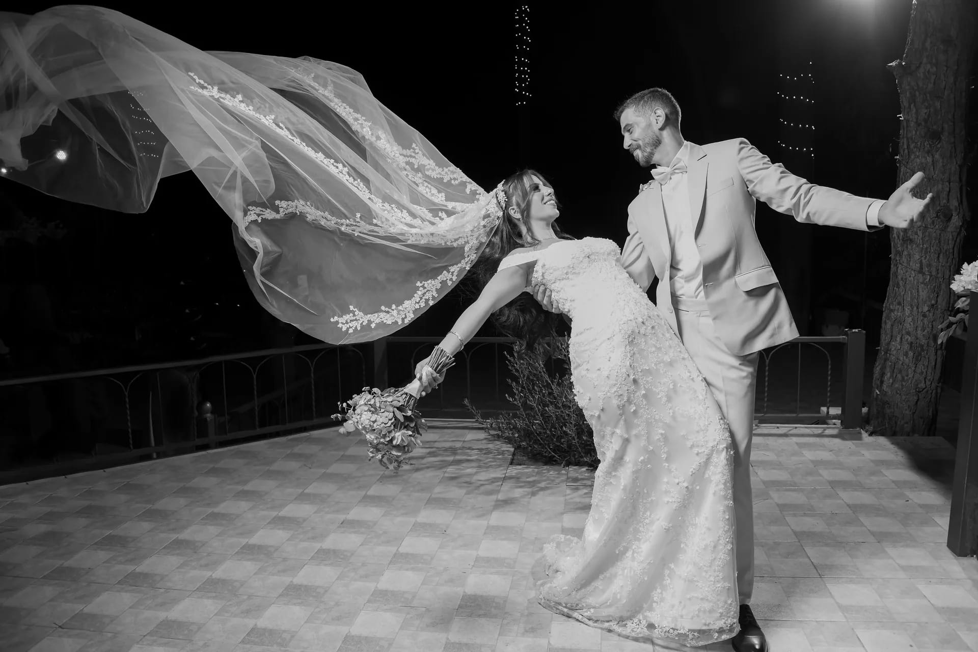 A bride's veil flying in the wind as the couple dances, in black and white