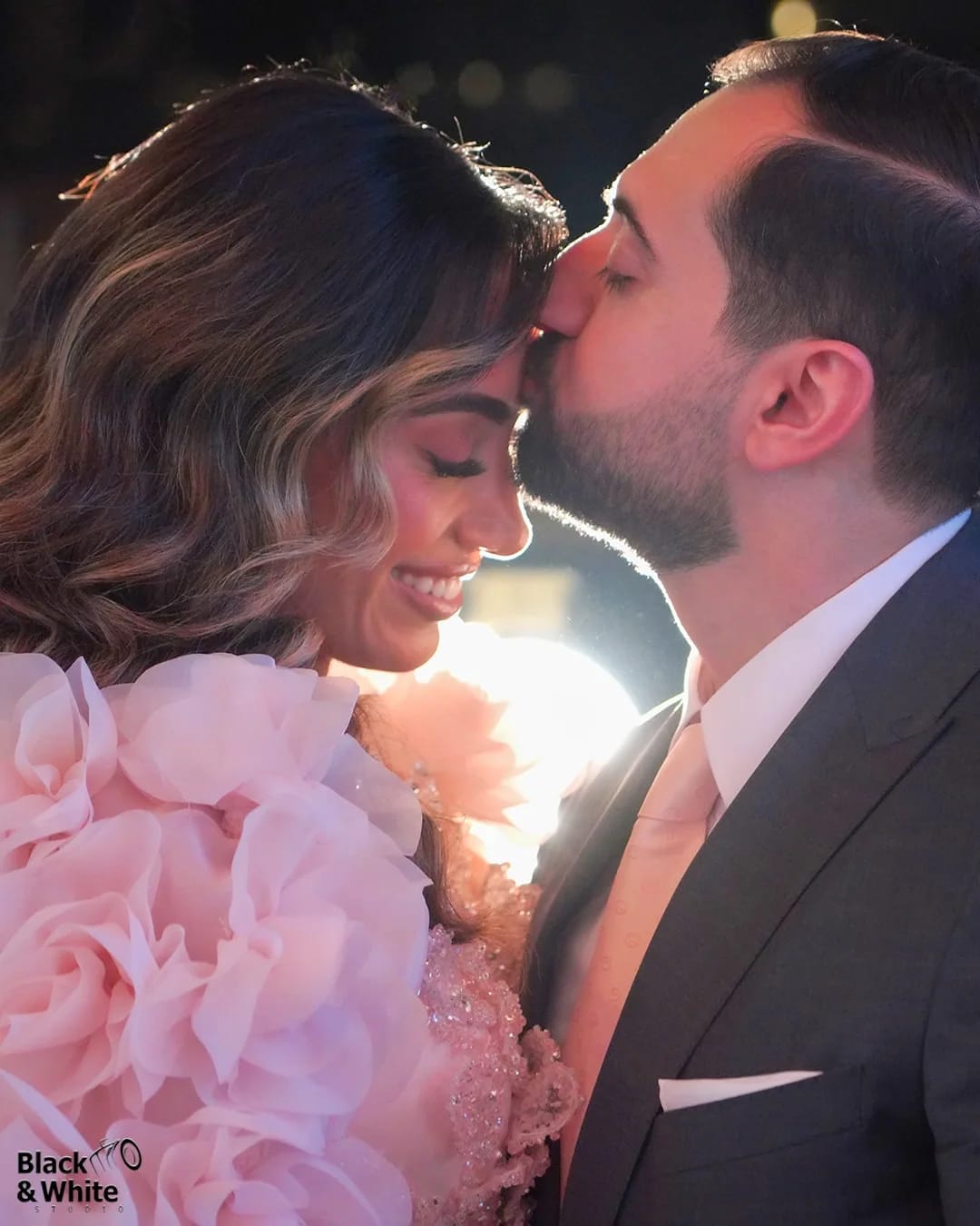 A groom kissing his bride's forehead in golden light