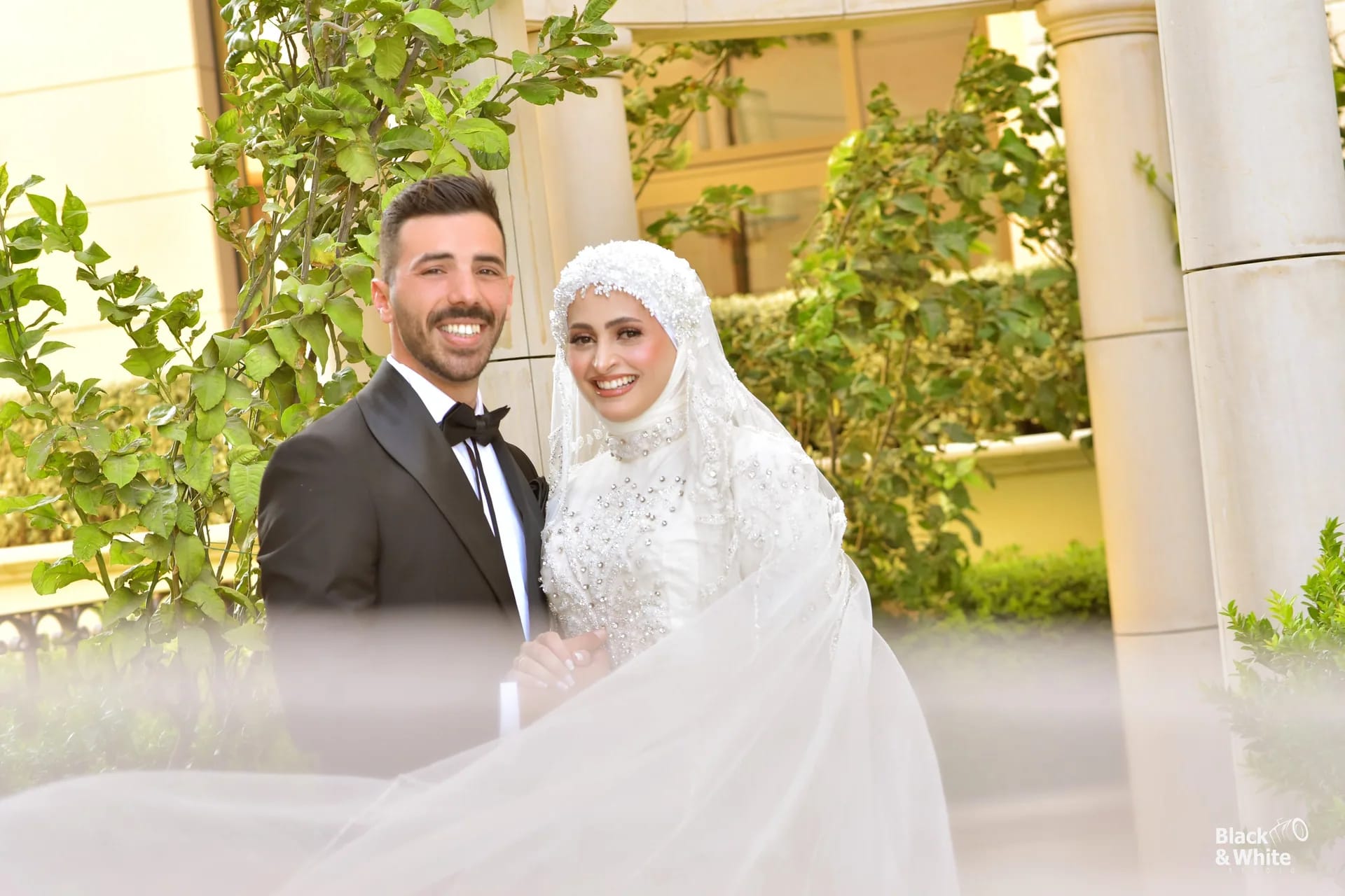 A groom and bride in a garden of white columns and greenery