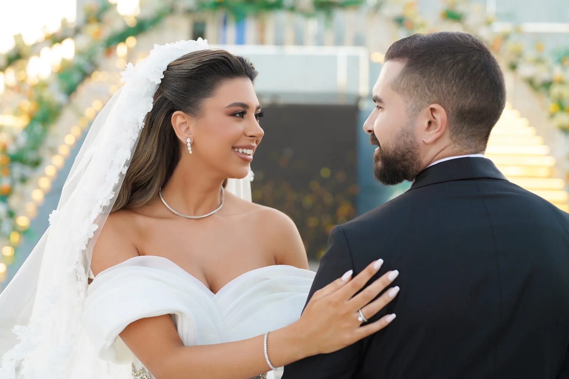 A bride's hand resting on her groom's shoulder under a floral arch