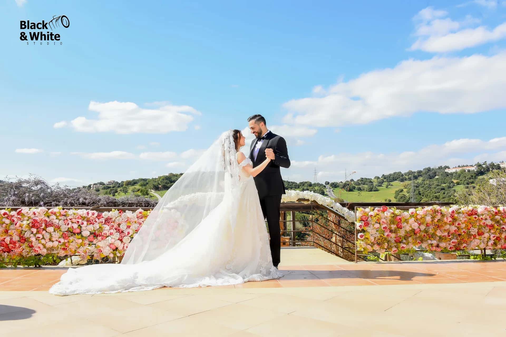 A couple on a terrace above a field of roses, under a blue sky
