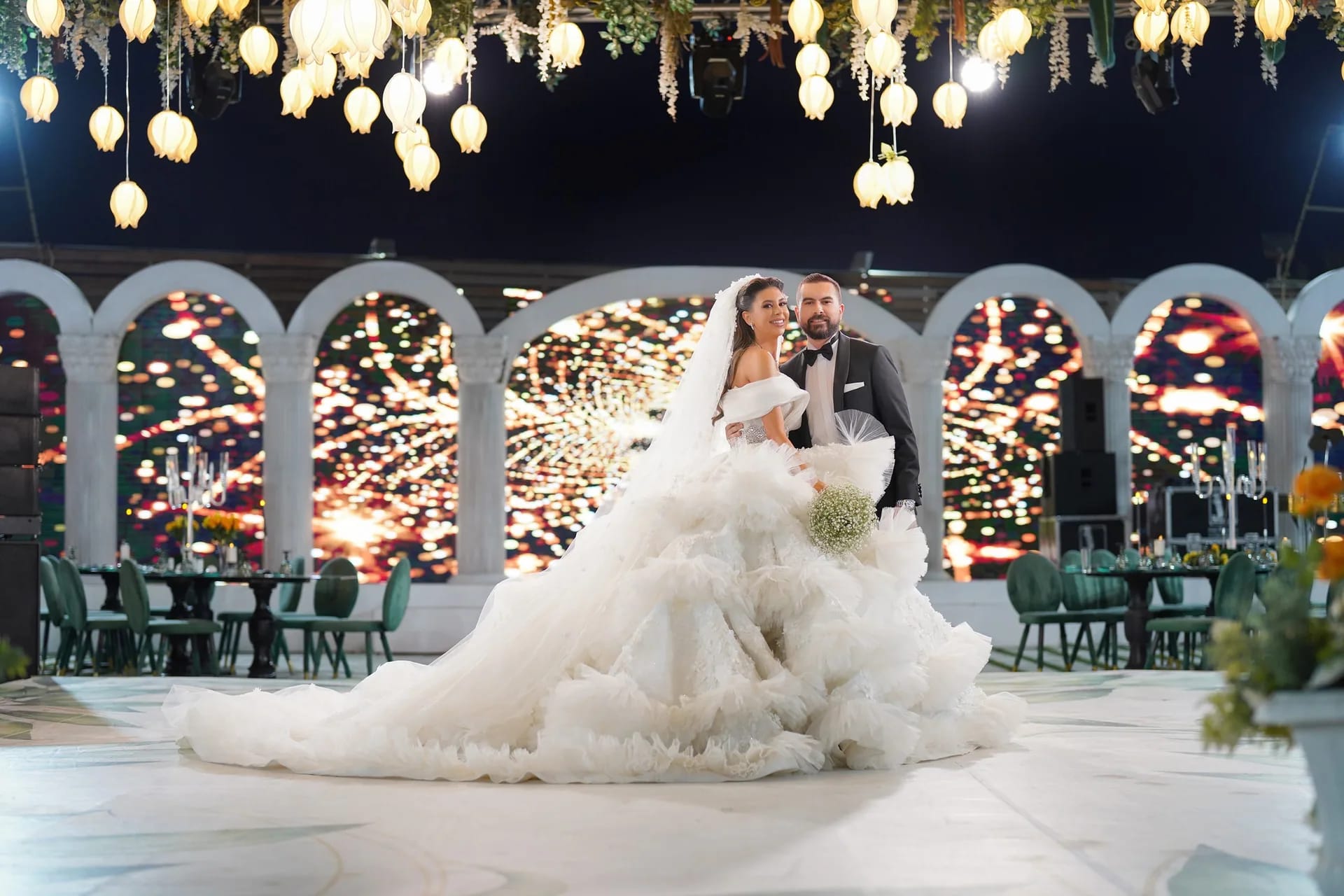 A bride in a full gown under strings of light at night