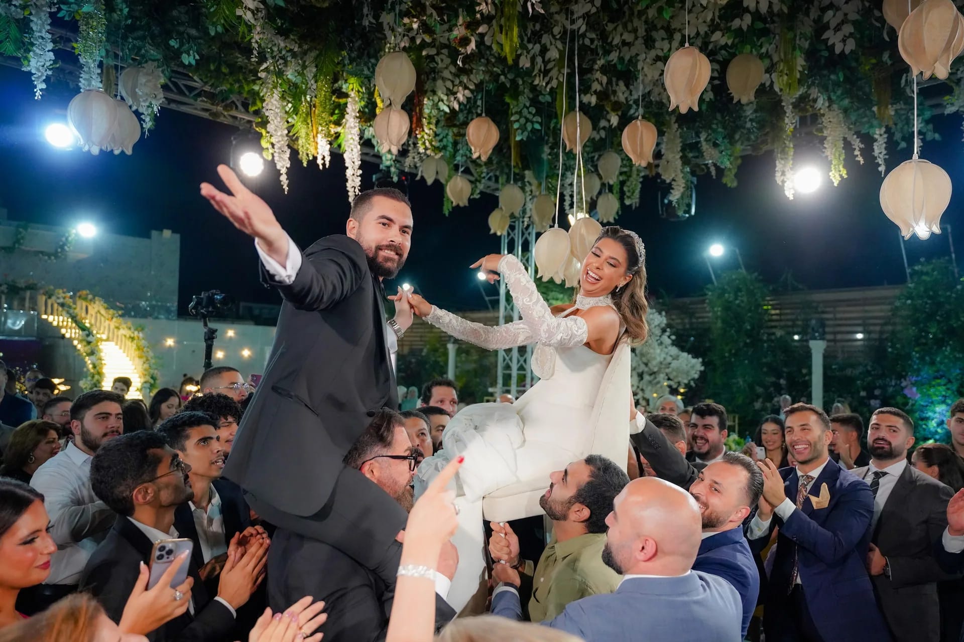 Guests lifting the groom and bride above a crowd at night