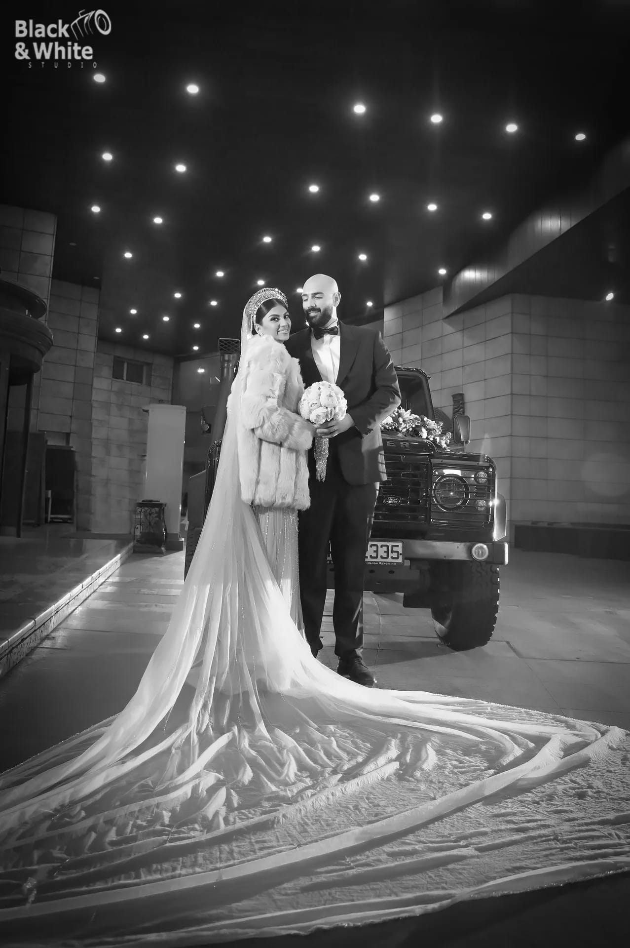 A bride's long train in front of the wedding car at night, in black and white