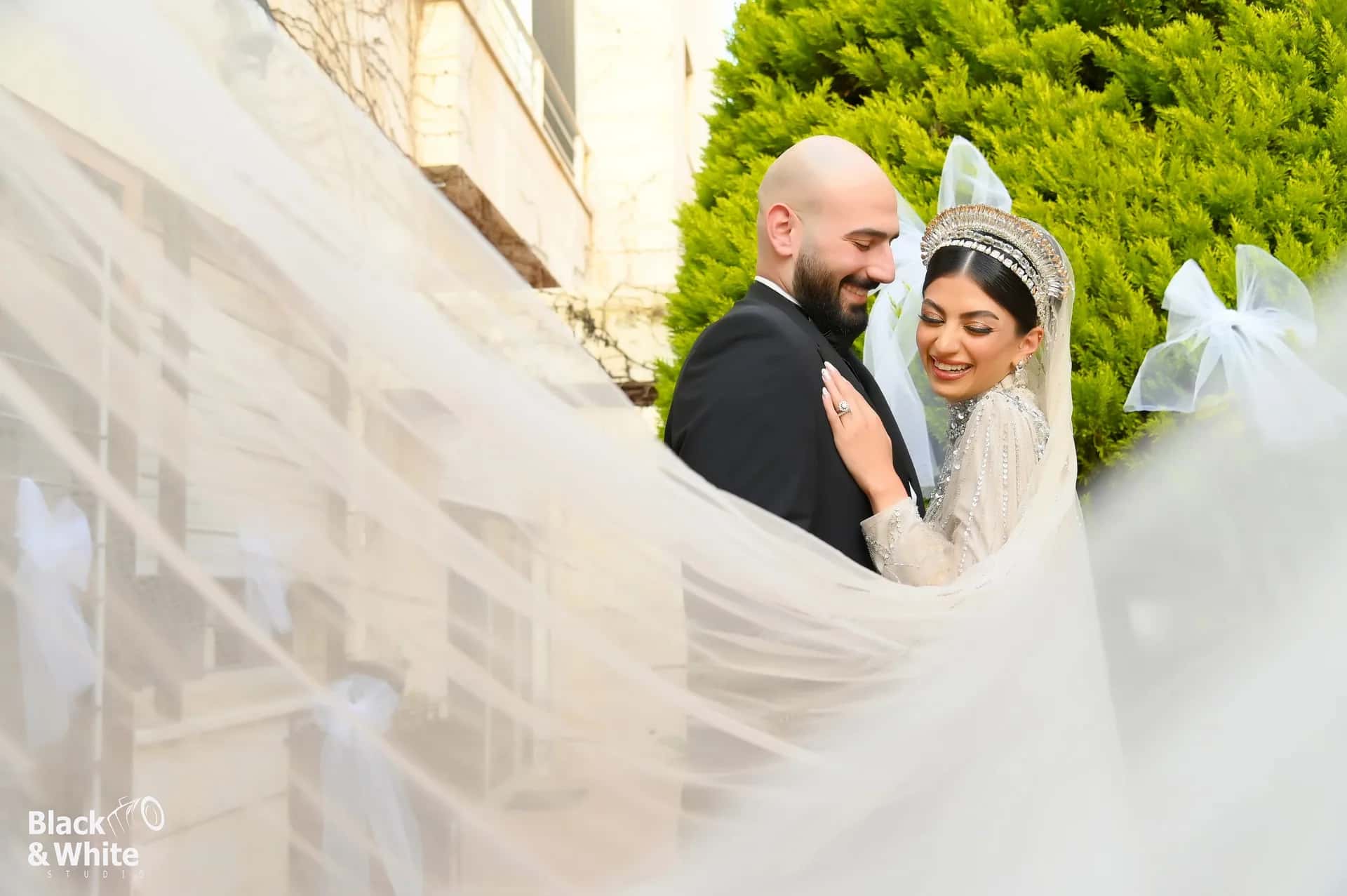 A groom and bride wrapped in a long veil, laughing