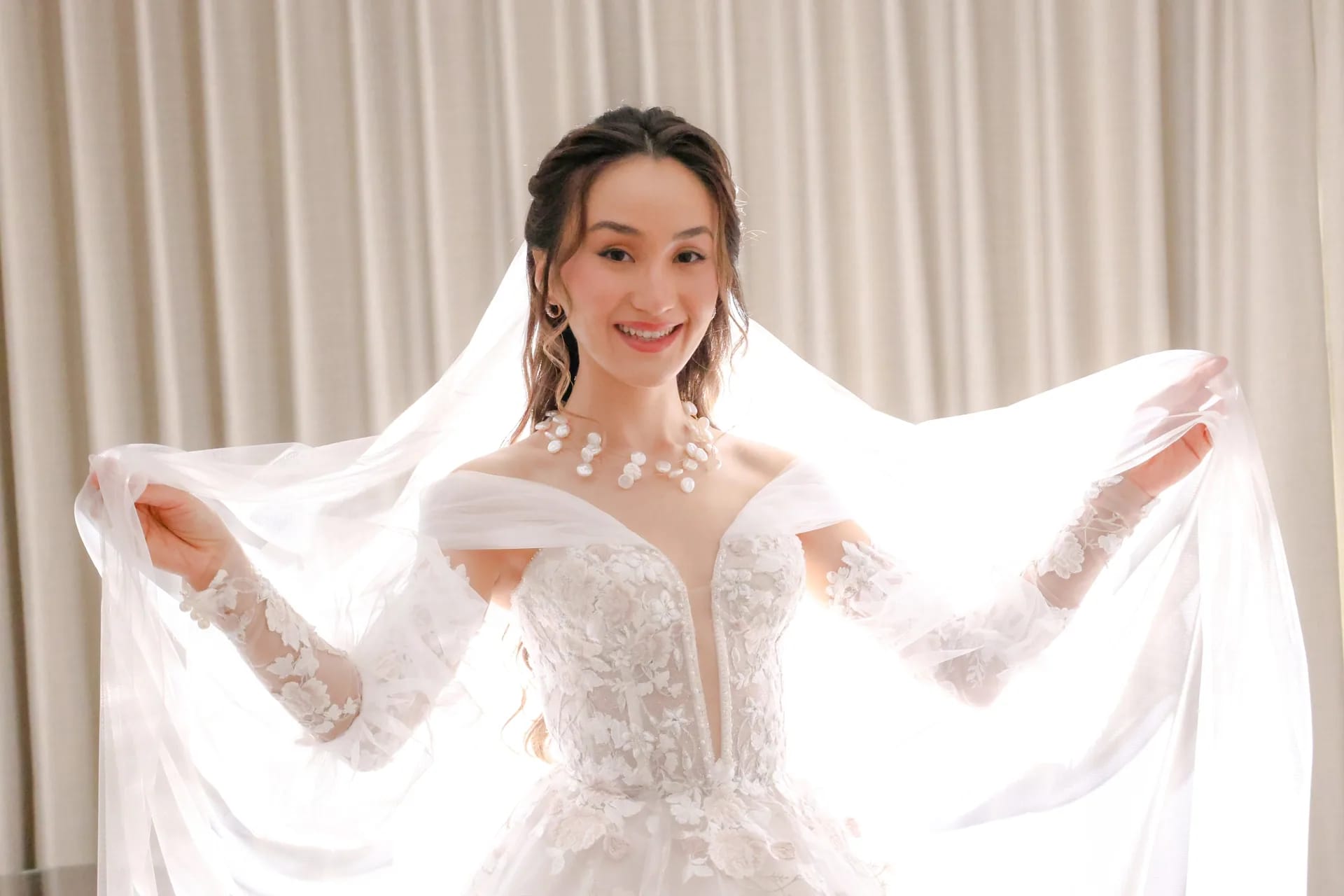 A bride smiling as she lifts her veil against soft window light