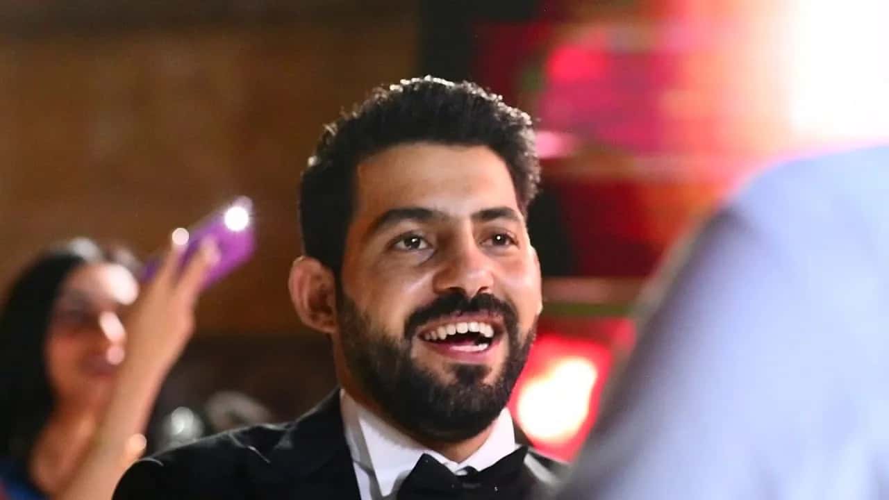 A groom laughing at his wedding party, guests filming on their phones behind him